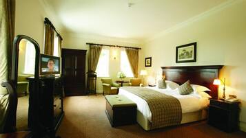 Habitación de hotel con cama, mesita de noche, lámpara, silla, escritorio, televisor y cortinas.