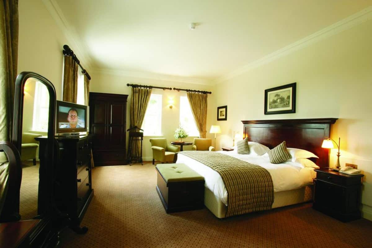 A hotel room with a bed, bedside tables, a desk with a computer, a chair, a lamp, and a window with curtains.
