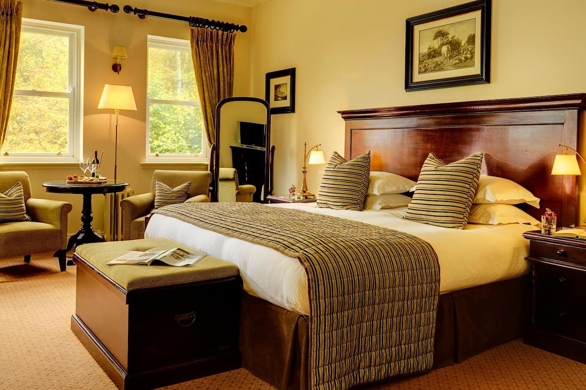 A hotel room with a large bed, two armchairs, a small table, and a nightstand.