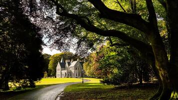 A large stone building with a symmetrical facade, surrounded by lush green trees and a well-maintained lawn.