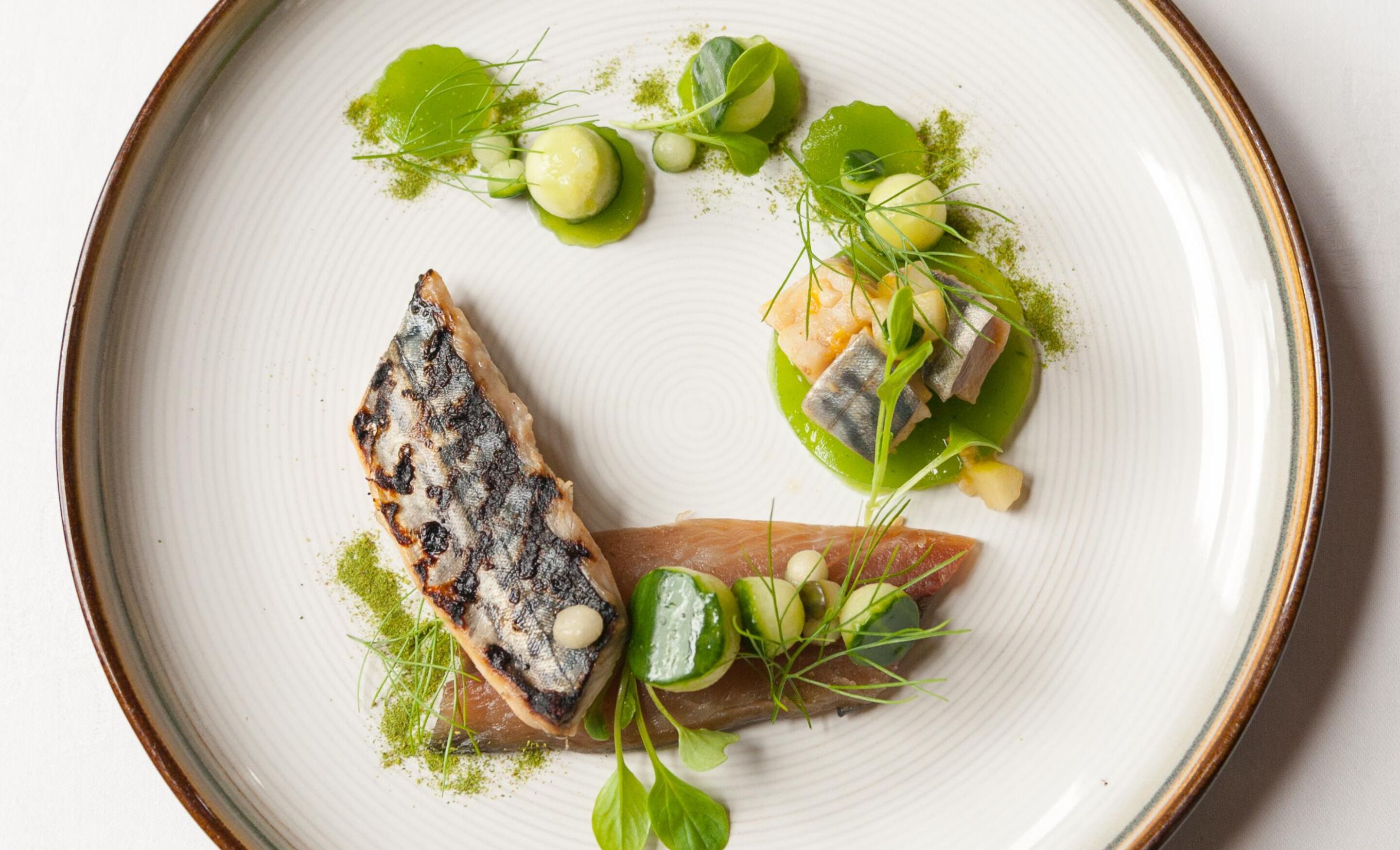 A plate with various food items including fish, greens, and garnishes.