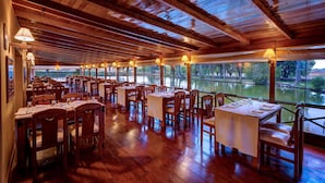 Un restaurante con mesas y sillas de madera, amplios ventanales con vistas a un cuerpo de agua y techo de madera.