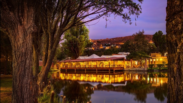 Un edificio junto al lago, con su reflejo en el agua, rodeado de árboles.