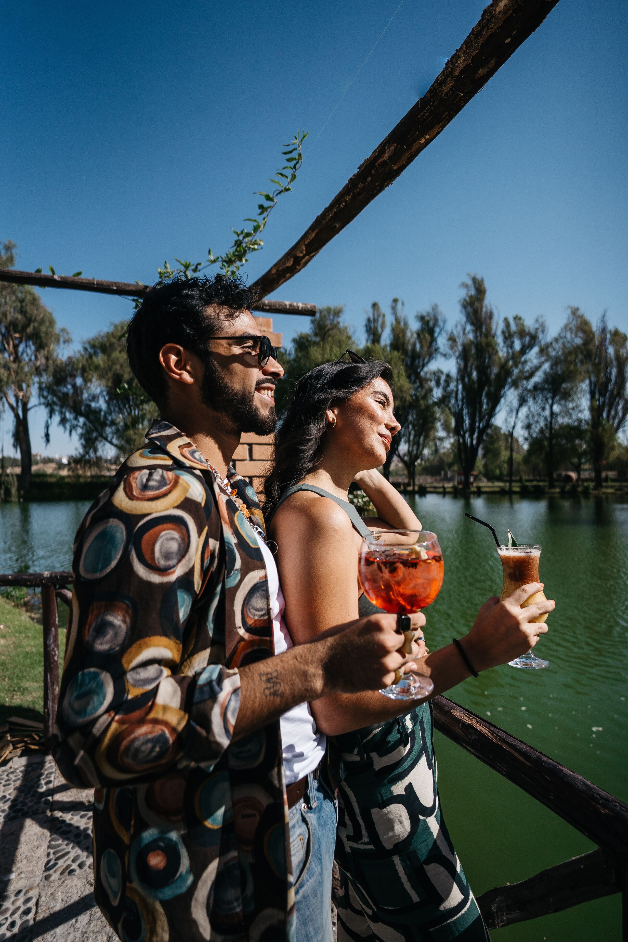 Dos personas junto al agua, sosteniendo bebidas.