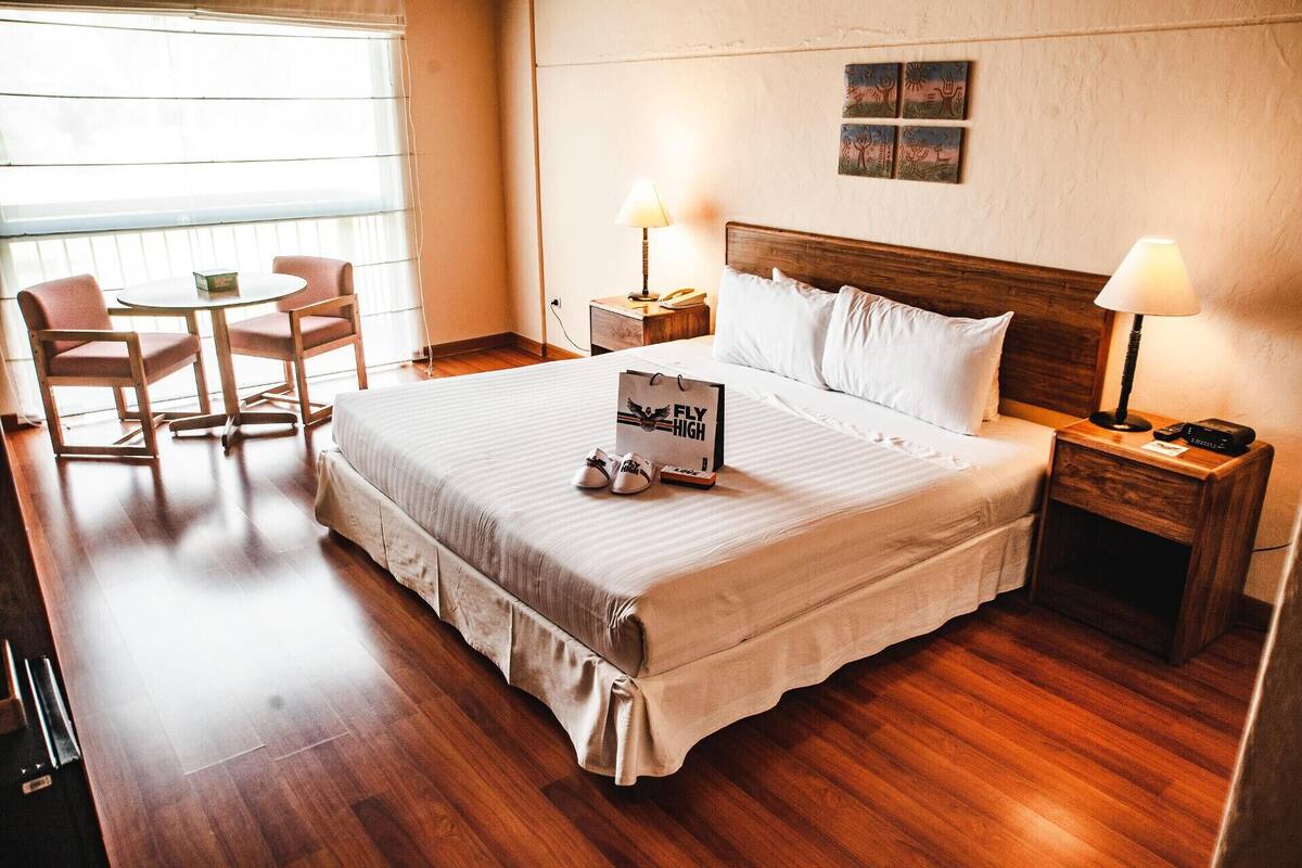 Quarto de hotel com uma cama, duas mesas de cabeceira, uma mesa com cadeiras e obras de arte na parede.