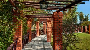 Un sendero de ladrillo con barandilla de madera, rodeado de follaje y árboles.