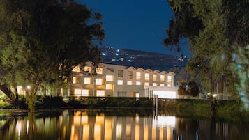 A multi-story building with a reflective pool in front, surrounded by trees.