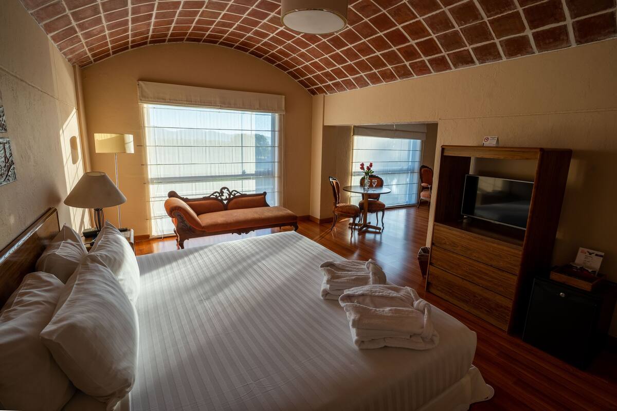 Quarto de hotel com uma cama grande, um sofá, uma TV e uma varanda com vista.