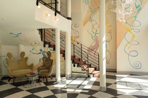 A spacious lobby with a checkered floor, a staircase with abstract wall art, and a seating area with a unique chair design. - Hôtel Le Magnifique (Paris)