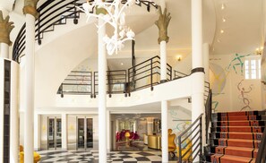 A multi-level interior with a checkered floor, a staircase with patterned carpet, and a central seating area with a round table. - Hôtel Le Magnifique (Paris)