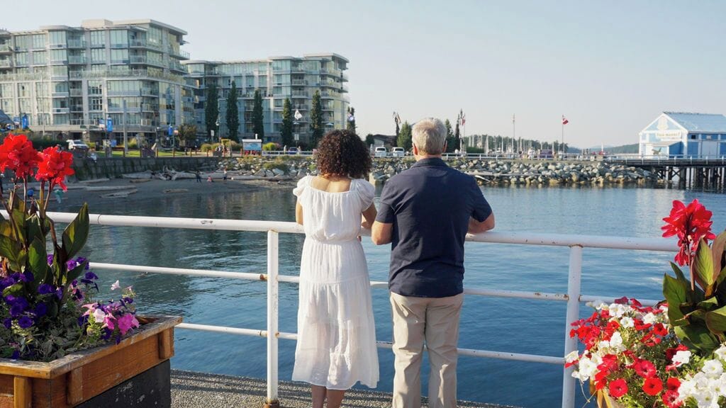Eine Uferpromenade mit modernen Gebäuden, einer Brüstung und Blumenkästen.