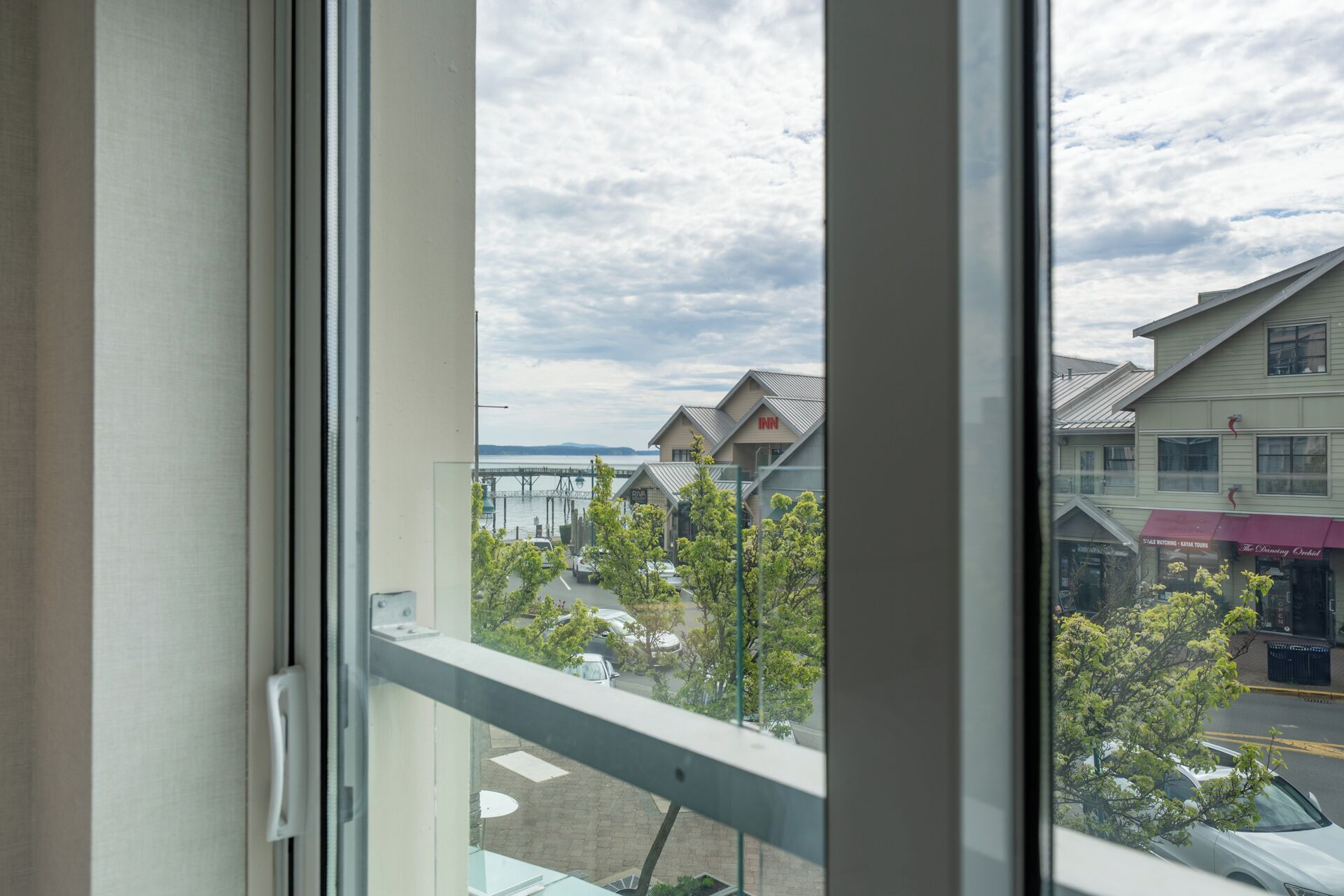 A view through a window with a metal railing, a clear sky, and buildings with signage including 'Inn' and 'The Dancing Orchid.'