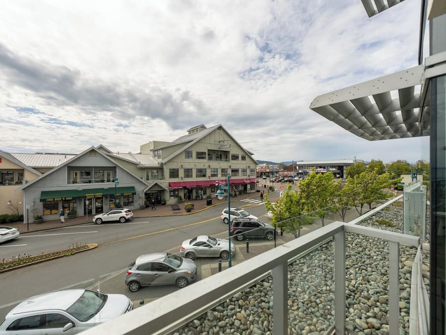A hotel with a flat roof, a visible outdoor seating area, and a street view with cars and shops.