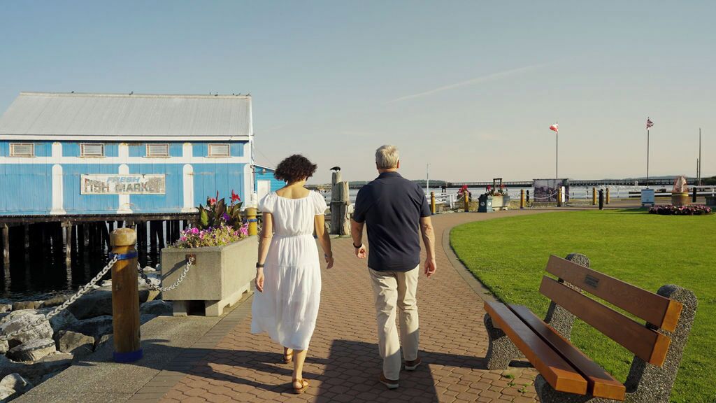 Un paseo marítimo con un banco, un edificio con un letrero y una zona verde.
