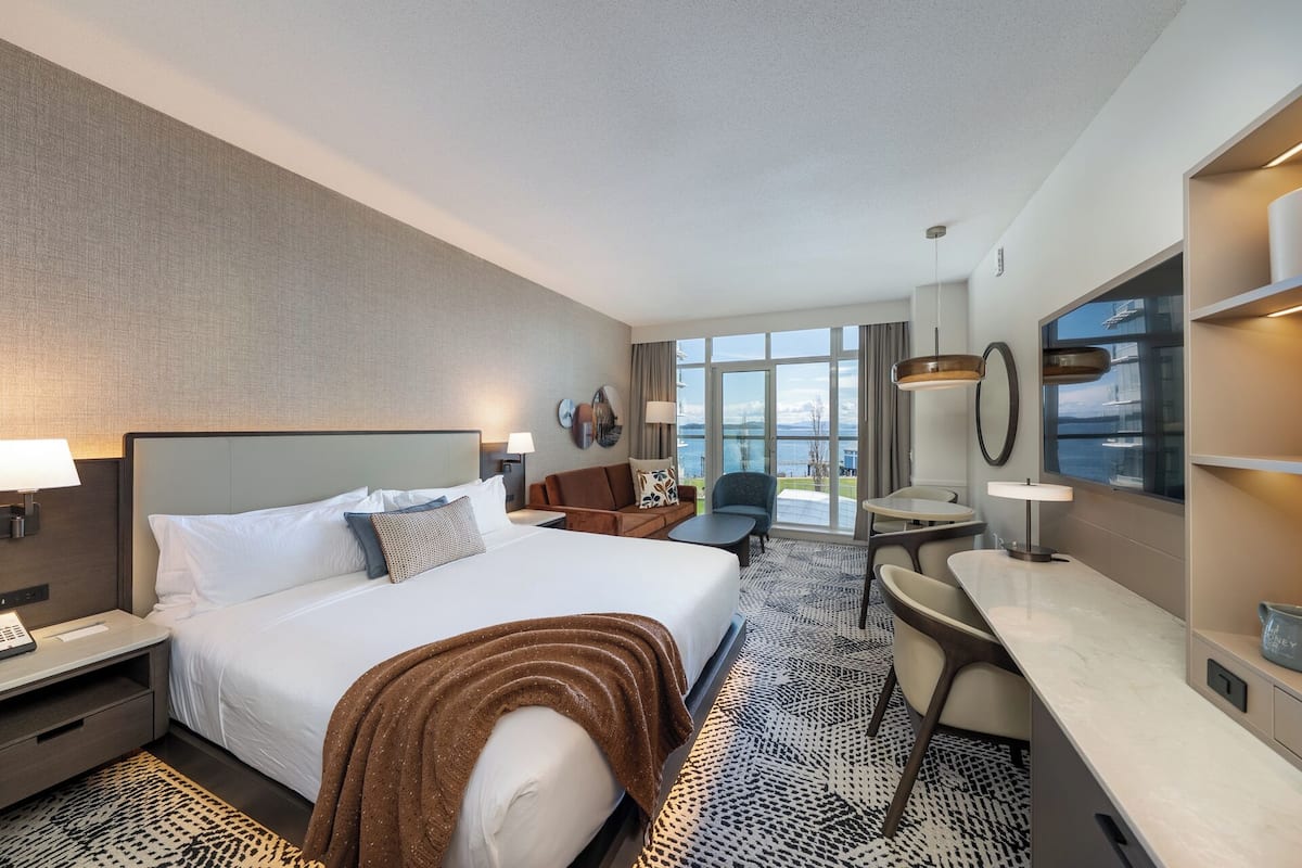 A hotel room with a large bed, a desk, a chair, and a view of the sea.