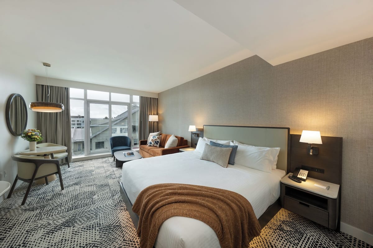 A hotel room with a large bed, a desk with a chair, a small table, and a sofa.