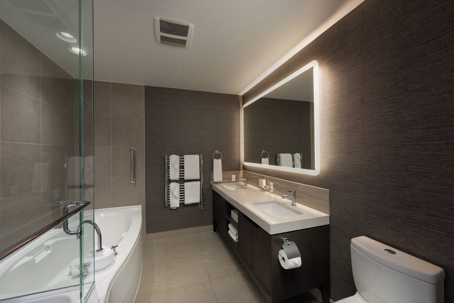 Un baño moderno con cabina de ducha de vidrio, bañera independiente, tocador con espejo grande y retrete.