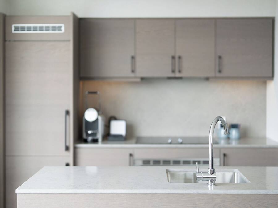 Una cocina moderna con encimera blanca, grifo de acero inoxidable y armarios de madera.
