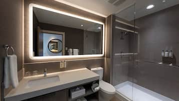 Un baño moderno con un espejo grande, un lavamanos, un inodoro y una zona de ducha con mampara de vidrio.
