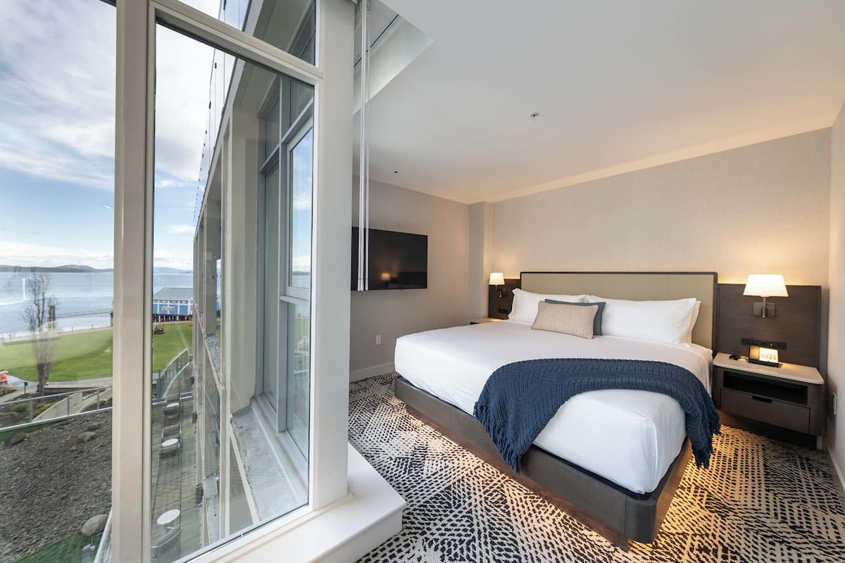 A hotel room with a large window, a bed, a TV, and a nightstand.