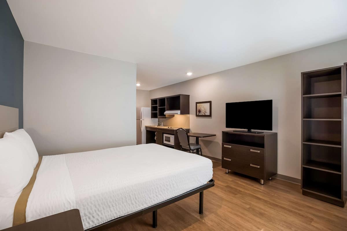 A hotel room with a bed, a desk with a computer, a TV, and built-in shelving.