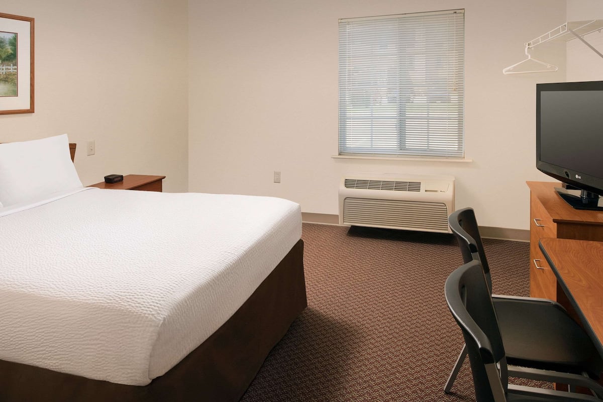 A hotel room with a bed, a desk, a chair, a television, and a window with blinds.
