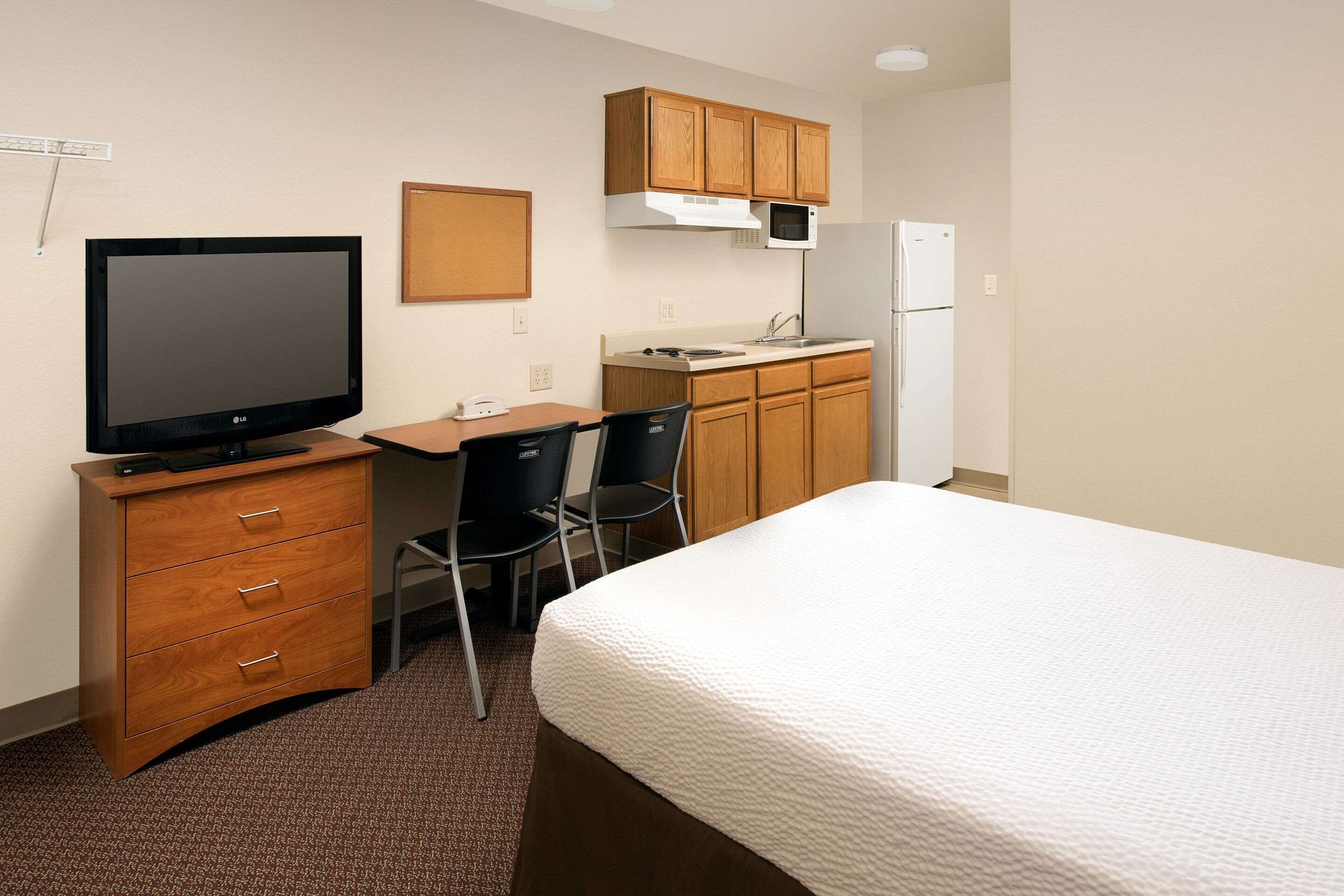 A hotel room with a bed, a desk with a television, a chair, a microwave, and a refrigerator.