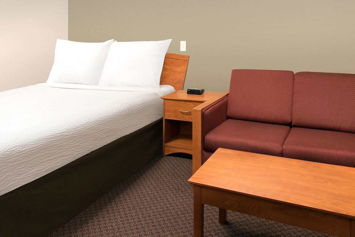 A hotel room with a bed, a wooden nightstand, a red sofa, and a small wooden table.