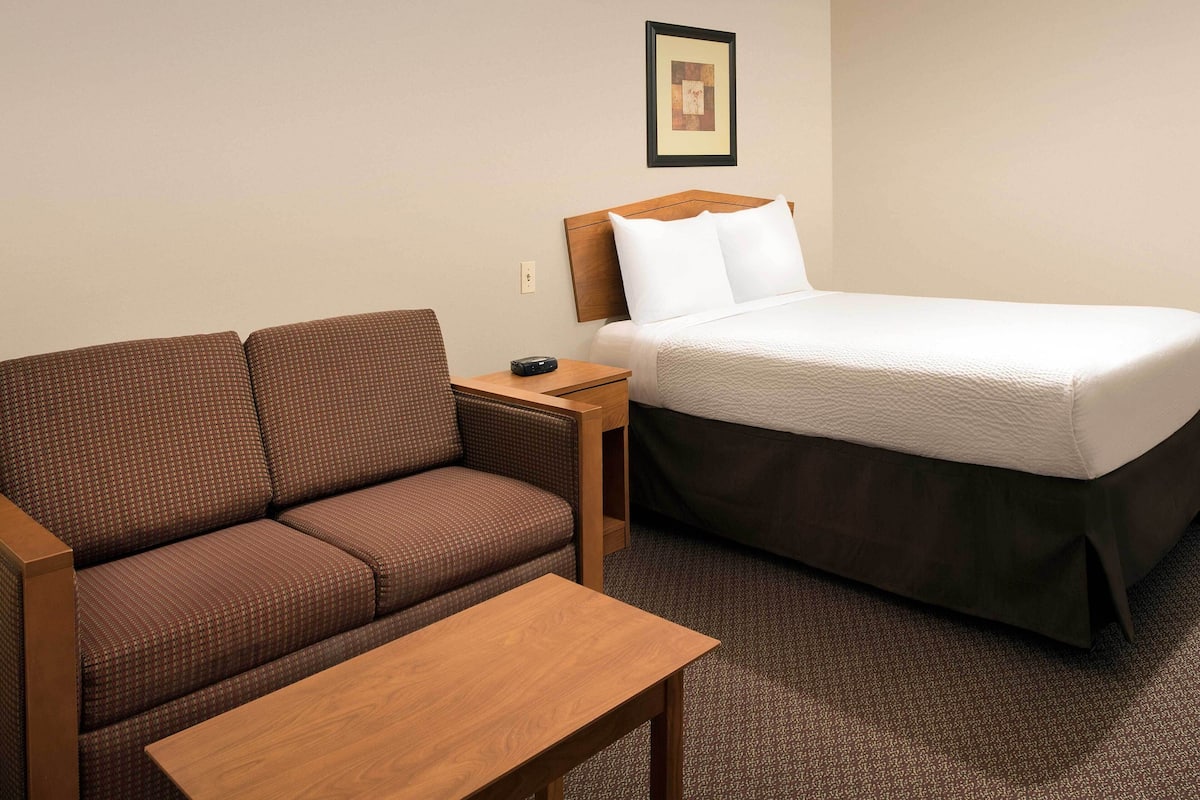 A hotel room with a brown sofa, a wooden table, and a bed with white bedding.