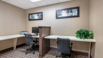 A modern office cubicle with two desks, each with a computer and chair. There are framed abstract artworks on the walls.