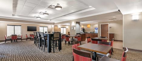 A hotel lobby with multiple seating areas, a reception desk, and a kitchen in the background.