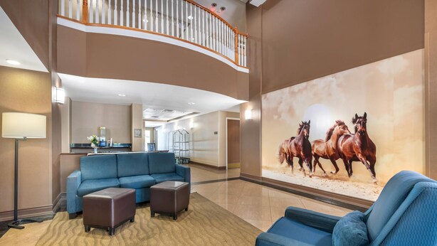 Eine großzügige Lobby mit einem blauen modularen Sofa, einem kleinen Hocker und einem großen Wandbild von Pferden.