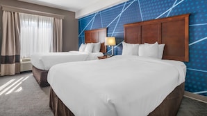 Ein Hotelzimmer mit zwei Betten, einem großen Fenster mit Vorhängen und einer blauen Wand mit Muster.