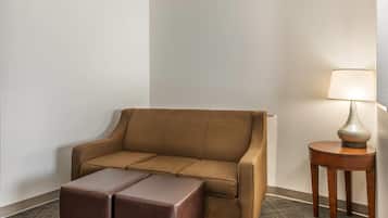 Una habitación de esquina con un sofá marrón, un reposapiés a juego y una pequeña mesa de madera con una lámpara.
