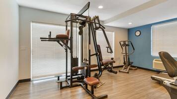Un gimnasio con una máquina de entrenamiento multifuncional, una cinta de correr y un reloj de pared.