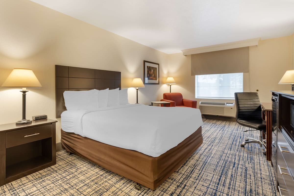 Ein Hotelzimmer mit einem großen Bett, Nachttischen mit Lampen, einem Schreibtisch mit Stuhl und einem Fenster mit Jalousien.