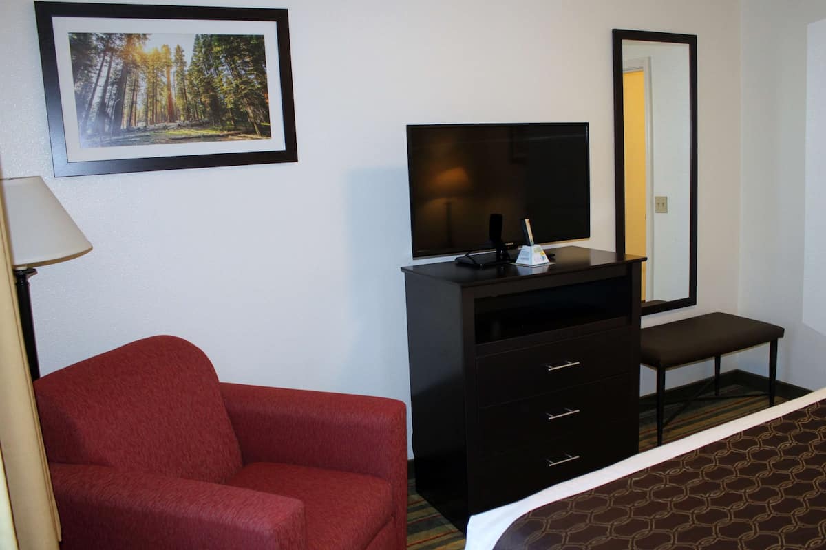 Ein Hotelzimmer mit einem roten Sofa, einem Fernseher auf einer Kommode, einem Spiegel und einem Bilderrahmen mit einem Waldfoto.
