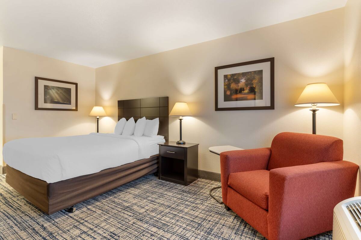 Ein Hotelzimmer mit einem Bett, zwei Nachttischen mit Lampen, einem Sessel und zwei gerahmten Bildern an den Wänden.