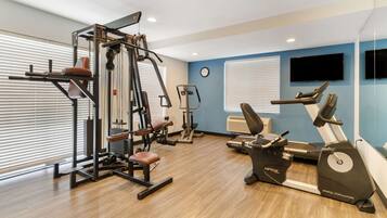 Une salle de sport équipée de machines de cardio, d’appareils de musculation et d’un téléviseur fixé au mur.