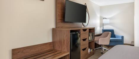 Ein Hotelzimmer mit einem Holztisch, einem an einer Holzplatte montierten Fernseher, einem blauen Sessel und einem Bett.