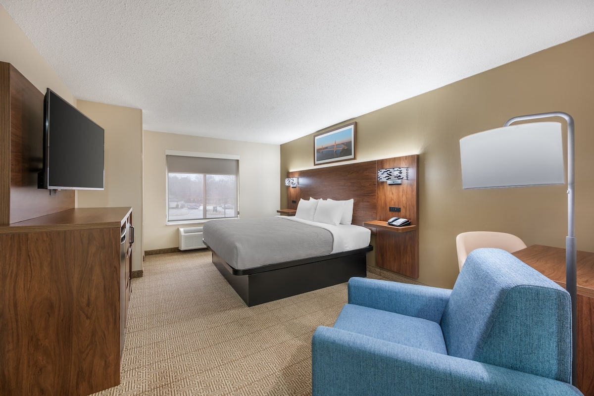 A hotel room with a bed, a desk, a chair, a TV, a bedside table, and a window.