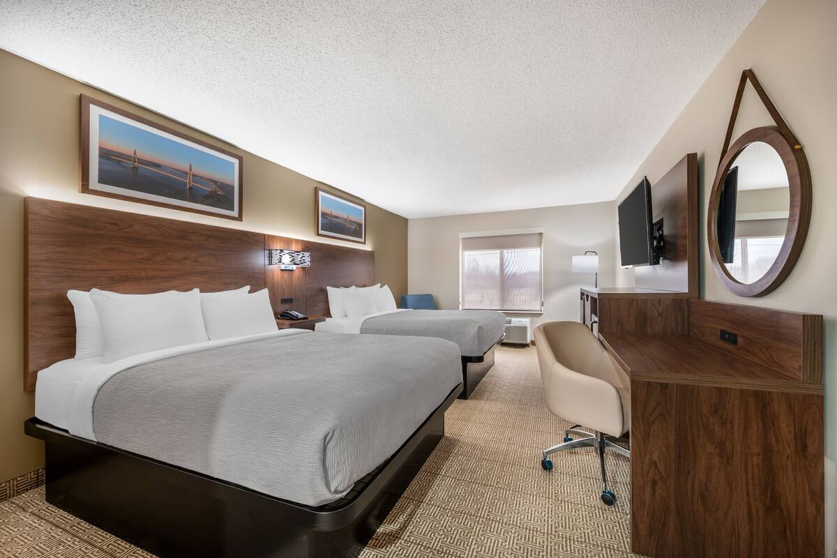 A hotel room with two beds, a desk, a chair, a TV, and a large mirror.