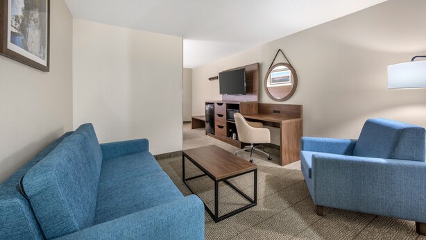 A hotel room with a blue sofa, a wooden coffee table, a desk with a computer and TV, and a small mirror on the wall.