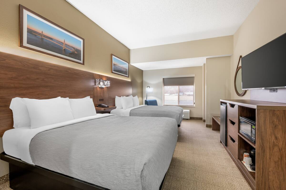 A hotel room with two beds, a TV, a desk with a chair, and a window.