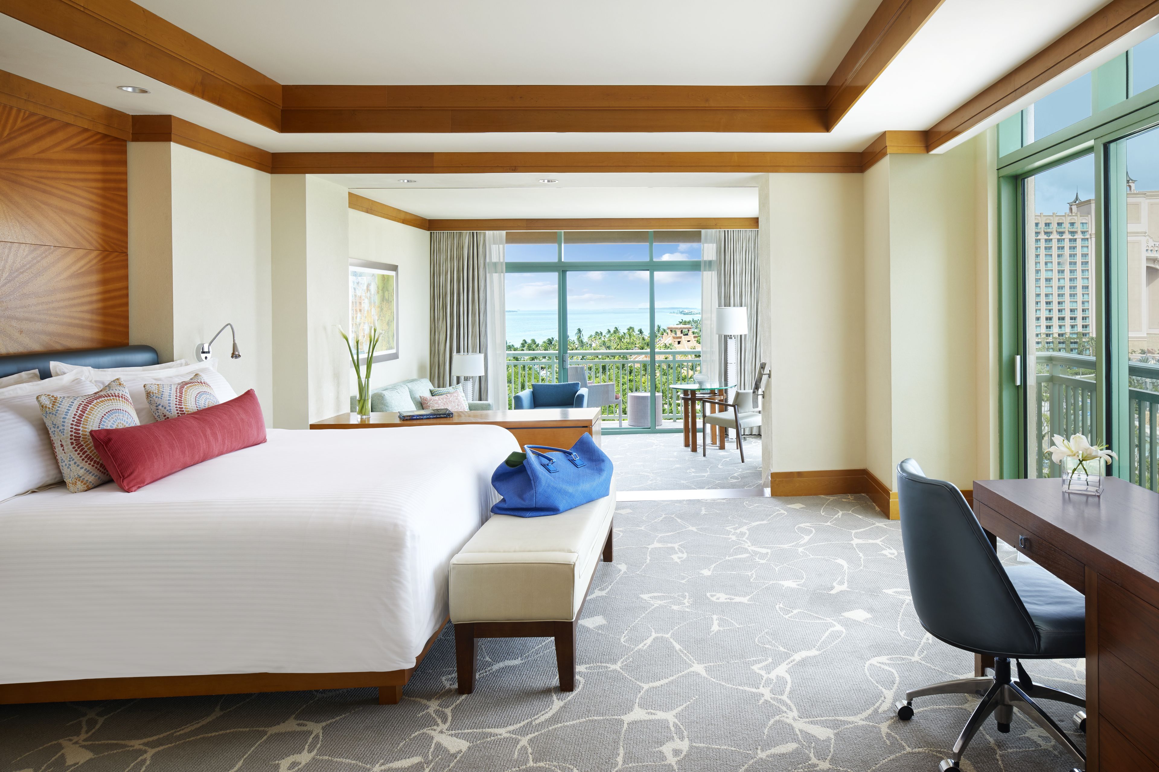 A hotel room with a large bed, a desk, a chair, and a balcony with a view.