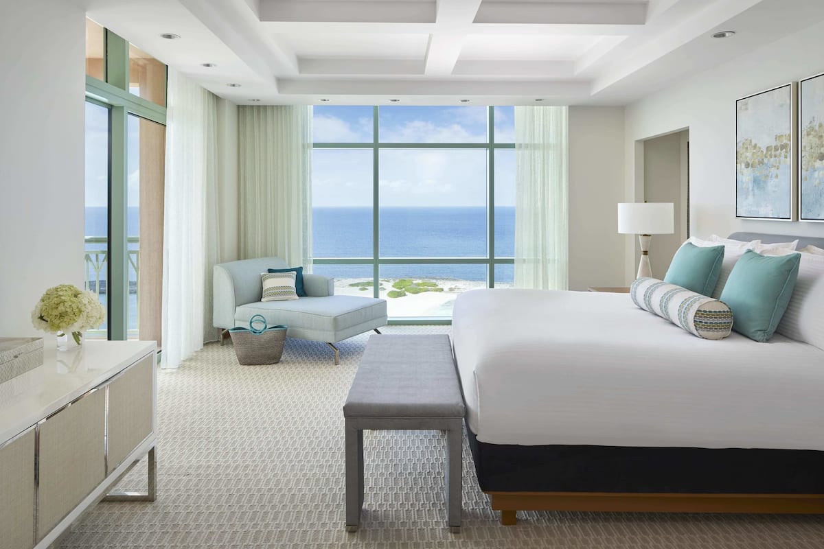 A hotel room with a large bed, a sofa, a small table, and a view of the ocean.