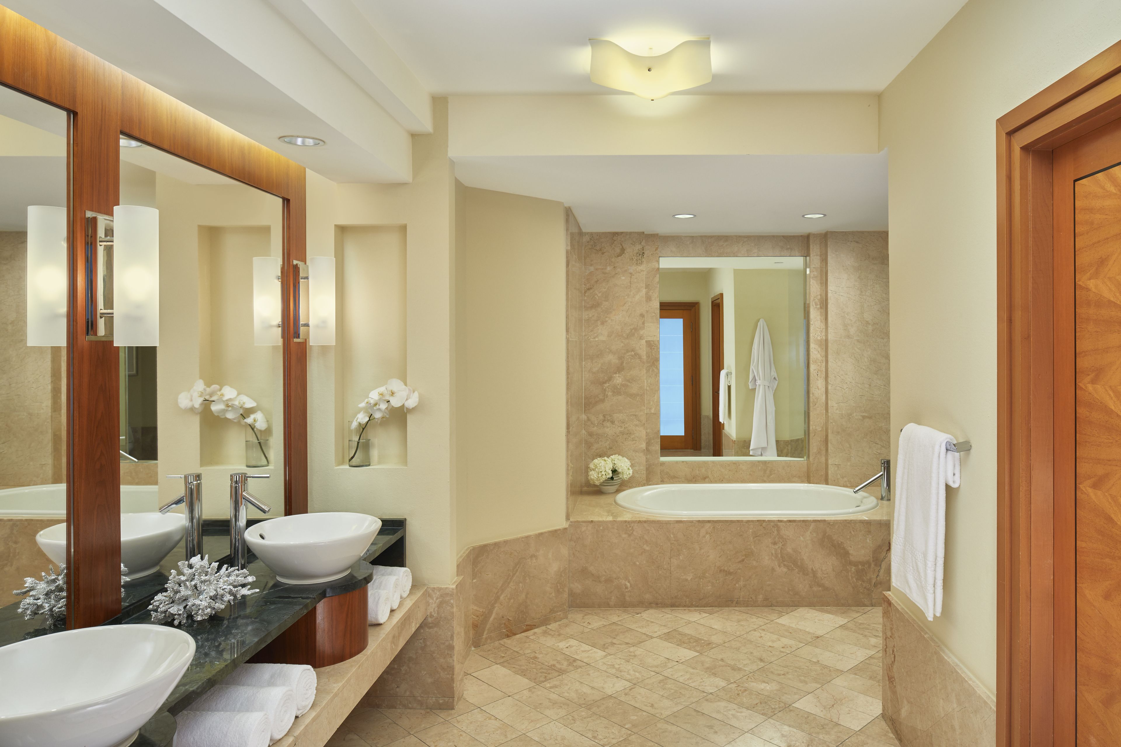 A modern bathroom with two sinks, a bathtub, and a large mirror.