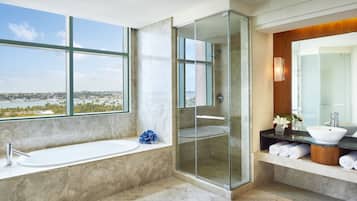 A modern bathroom with a large bathtub, a glass-enclosed shower, a vanity with a sink, and a view of a cityscape through large windows.