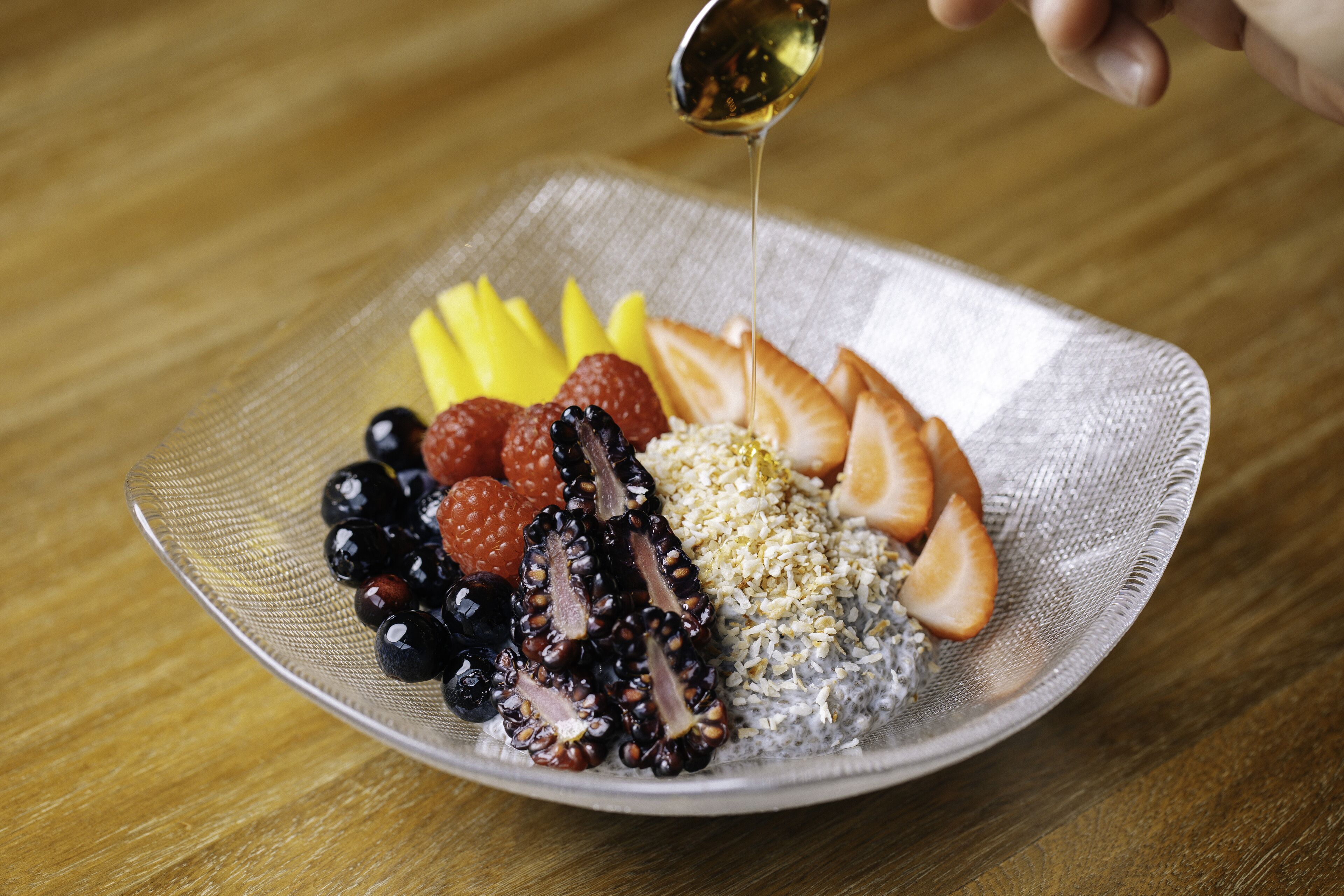 A plate with various fruits and a spoon pouring a liquid.