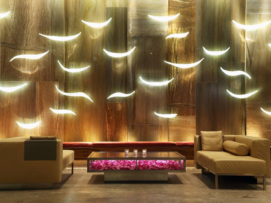 A modern lounge area with a sofa, a glass coffee table, and a wall with unique lighting fixtures.